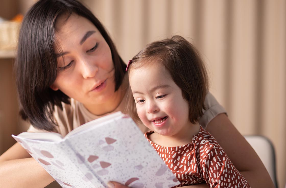 Cute baby girl with down syndrome with book studying